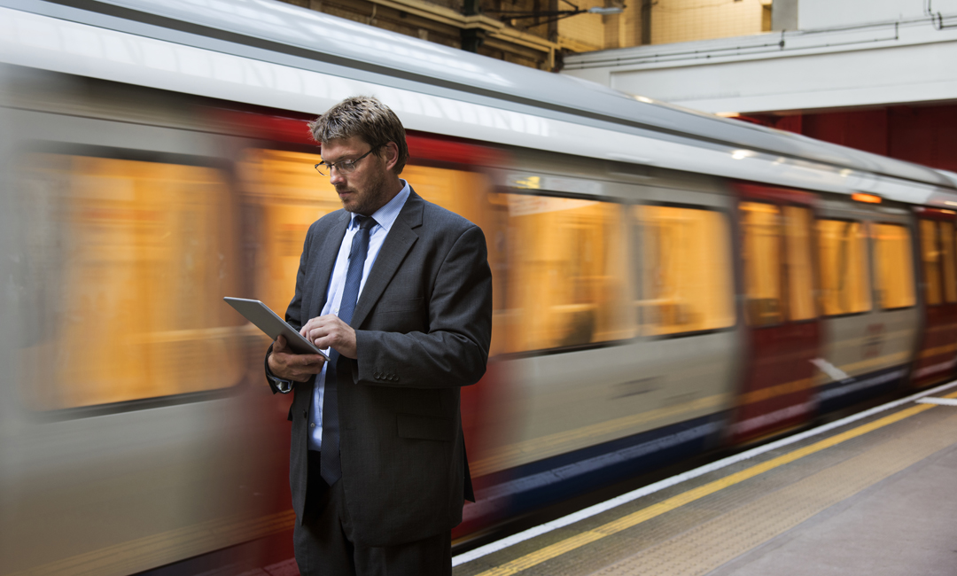Man looking at tablet with train passing behind